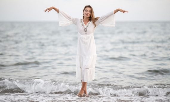 Elegant woman in white dress standing at the seaside, embracing the serene ocean backdrop.