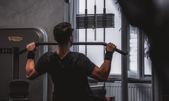 Back view of a man exercising with lat pulldown machine in the gym.